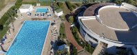 Piscina e edificio circolare visti dall'alto, con campi da tennis dietro.